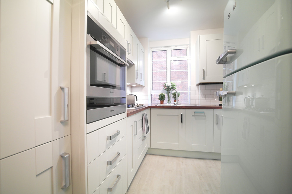 Photo of a medium sized rural l-shaped enclosed kitchen in London with shaker cabinets, green cabinets, wood worktops, white splashback and no island.