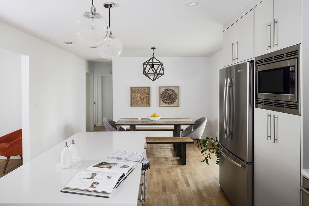 Example of a mid-sized 1950s l-shaped light wood floor eat-in kitchen design in Austin with a farmhouse sink, flat-panel cabinets, gray cabinets, glass countertops, white backsplash, subway tile backsplash, stainless steel appliances and an island