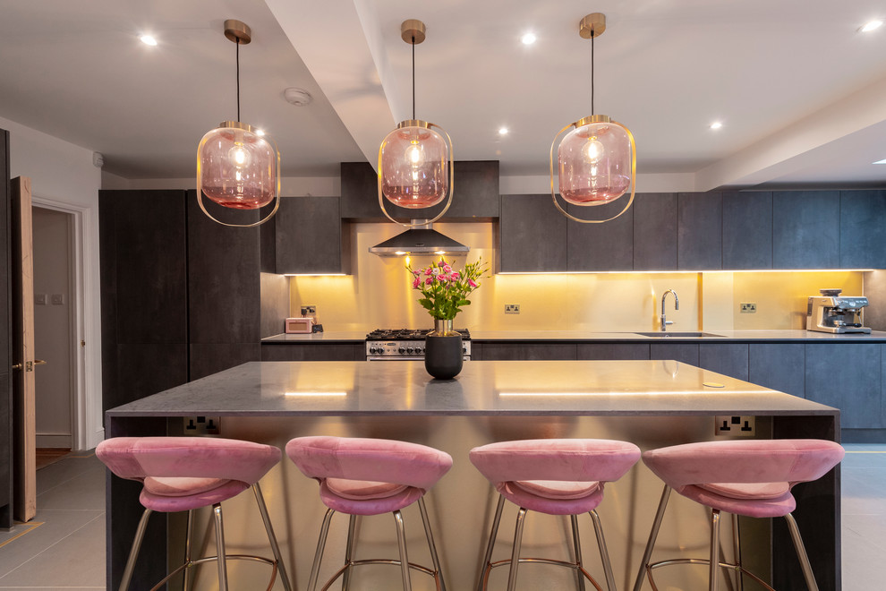 This is an example of a contemporary grey and pink galley kitchen in London with a submerged sink, flat-panel cabinets, grey cabinets, stainless steel appliances, an island and grey floors.