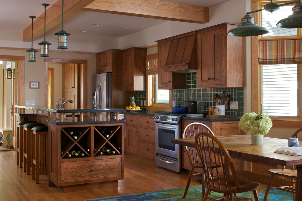 Exempel på ett amerikanskt svart svart kök, med skåp i mörkt trä, grönt stänkskydd, stänkskydd i keramik, rostfria vitvaror, en köksö, en undermonterad diskho, luckor med infälld panel, bänkskiva i täljsten, mellanmörkt trägolv och brunt golv