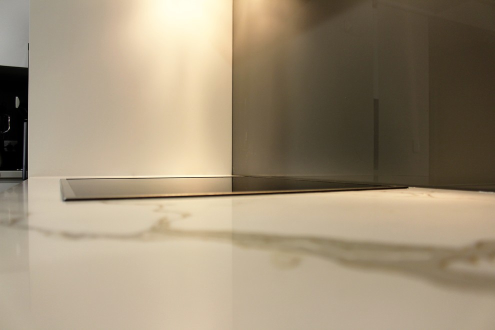 Foto på ett mellanstort kök, med en undermonterad diskho, släta luckor, vita skåp, bänkskiva i kvarts, brunt stänkskydd, glaspanel som stänkskydd, rostfria vitvaror, ljust trägolv och en halv köksö