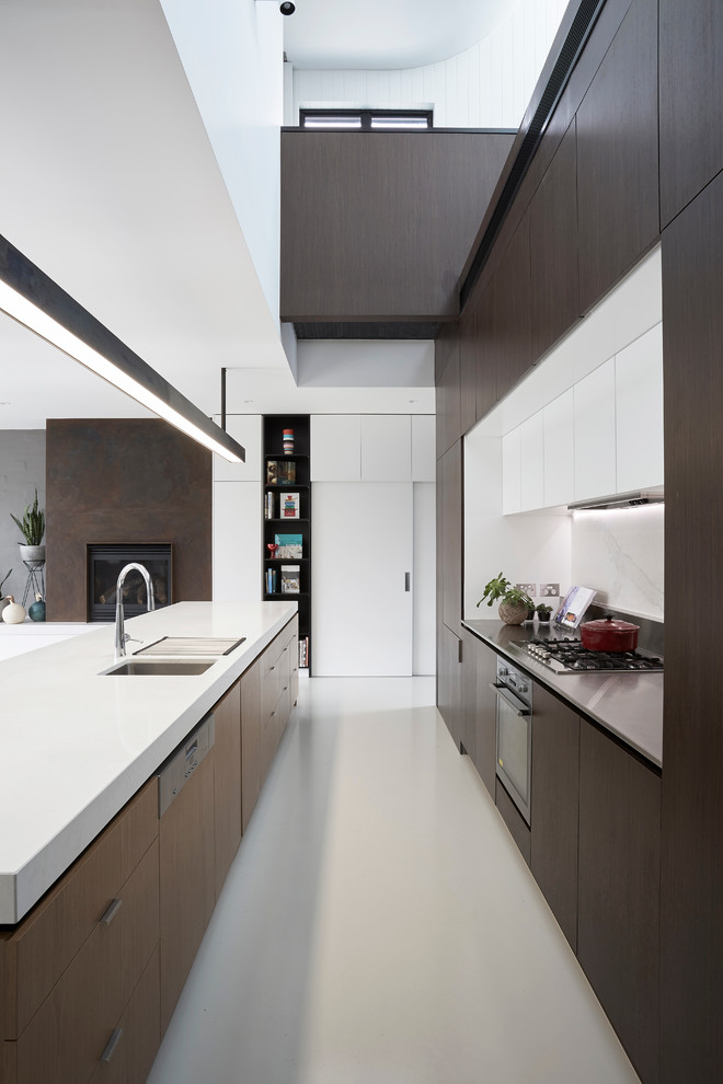 Mid-sized trendy galley concrete floor eat-in kitchen photo in Melbourne with an undermount sink, flat-panel cabinets, brown cabinets, stainless steel countertops, white backsplash, stone slab backsplash, stainless steel appliances and an island