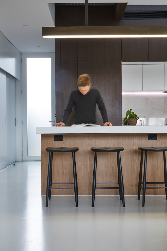 Inspiration for a medium sized contemporary galley kitchen/diner in Melbourne with flat-panel cabinets, dark wood cabinets, stone slab splashback, concrete flooring, an island, a submerged sink, composite countertops, grey splashback and stainless steel appliances.
