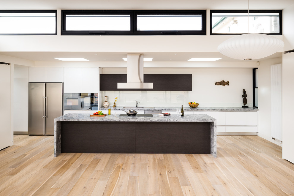 Inspiration for a large modern galley kitchen in Melbourne with flat-panel cabinets, white cabinets, marble worktops, white splashback, glass sheet splashback, stainless steel appliances, light hardwood flooring, an island and a built-in sink.