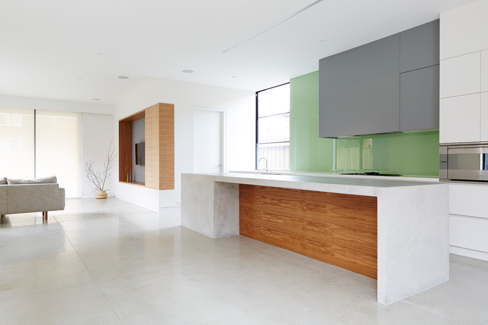 Bild på ett mellanstort funkis kök, med en dubbel diskho, släta luckor, vita skåp, bänkskiva i betong, grönt stänkskydd, glaspanel som stänkskydd, rostfria vitvaror, betonggolv och en köksö