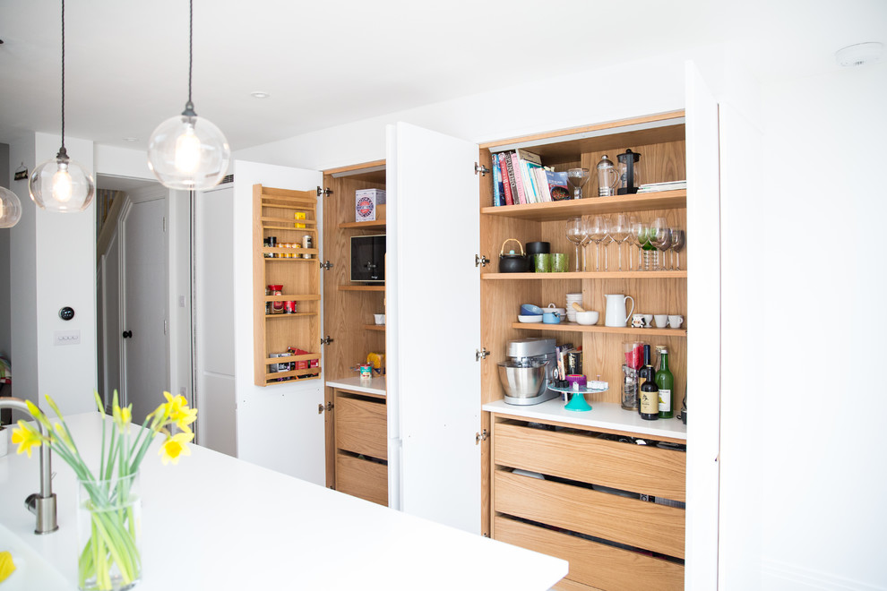 Inspiration for a medium sized modern galley open plan kitchen in London with an integrated sink, flat-panel cabinets, white cabinets, white splashback, light hardwood flooring, an island, brown floors, white worktops, composite countertops and stainless steel appliances.