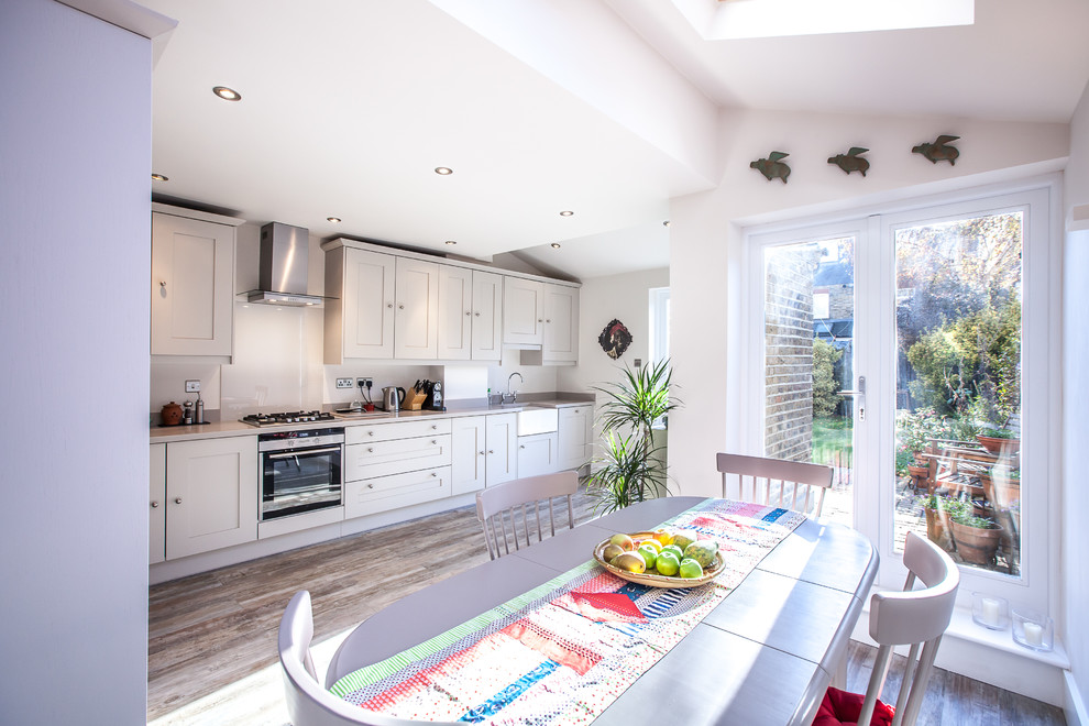 This is an example of a medium sized modern single-wall kitchen/diner in London with a belfast sink, shaker cabinets, beige cabinets, composite countertops, grey splashback, stone slab splashback, integrated appliances, painted wood flooring and no island.