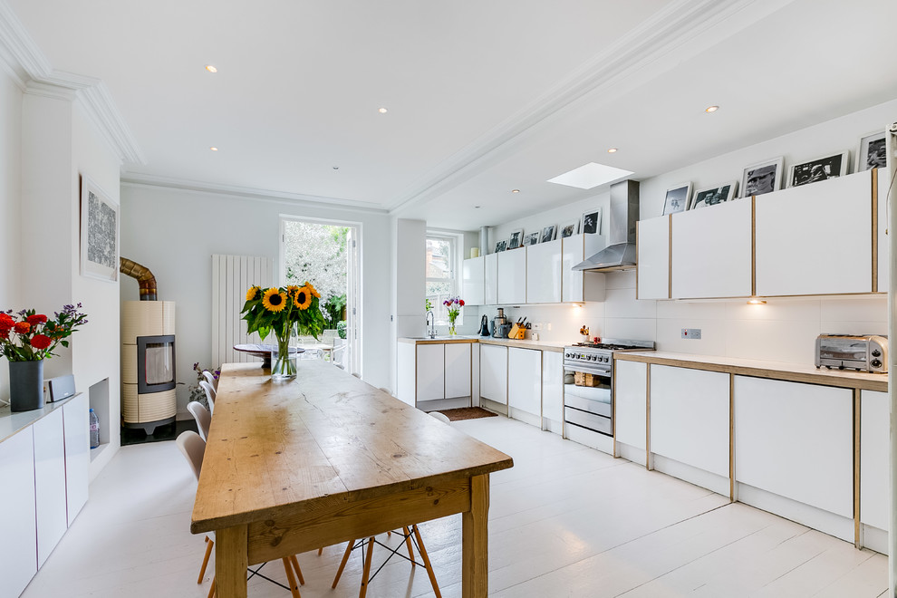 Photo of a medium sized country single-wall kitchen/diner in London with flat-panel cabinets, white cabinets, wood worktops, white splashback, stainless steel appliances, no island, white floors, white worktops and painted wood flooring.