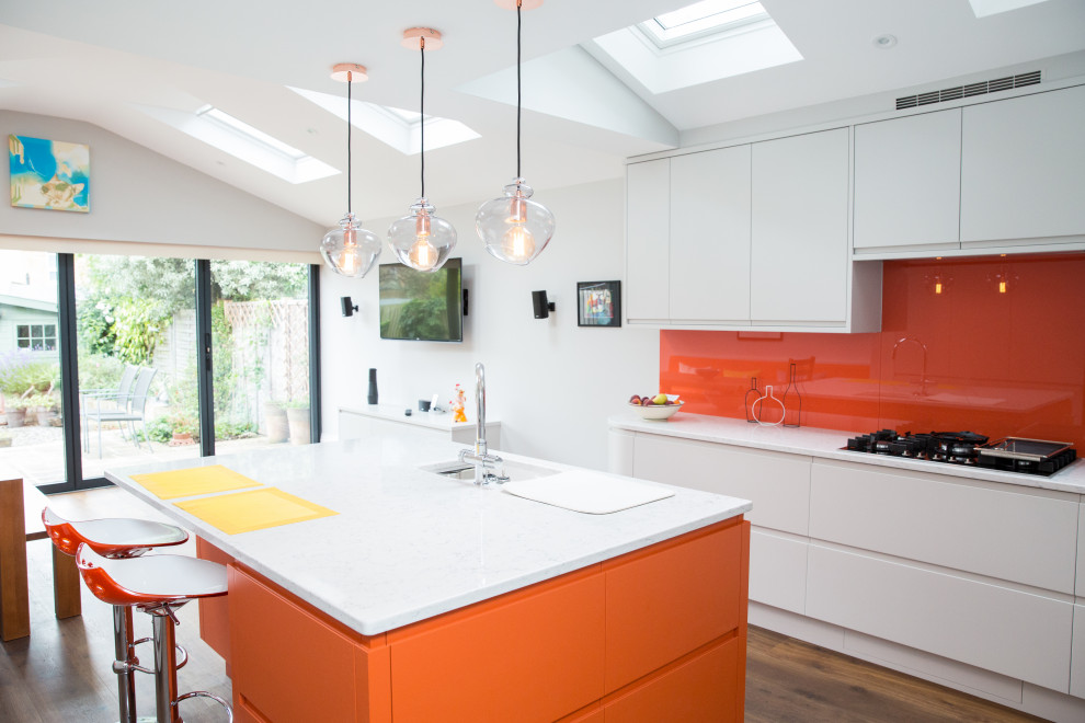 This is an example of a medium sized modern u-shaped open plan kitchen in London with a single-bowl sink, flat-panel cabinets, orange cabinets, composite countertops, orange splashback, glass tiled splashback, dark hardwood flooring, an island, brown floors and white worktops.