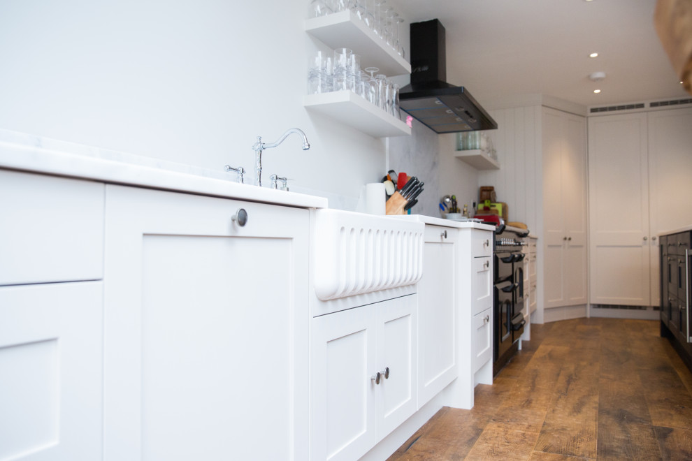 Foto di una cucina moderna di medie dimensioni con lavello sottopiano, ante in stile shaker, ante blu, top in superficie solida, elettrodomestici neri, parquet scuro, pavimento marrone e top bianco