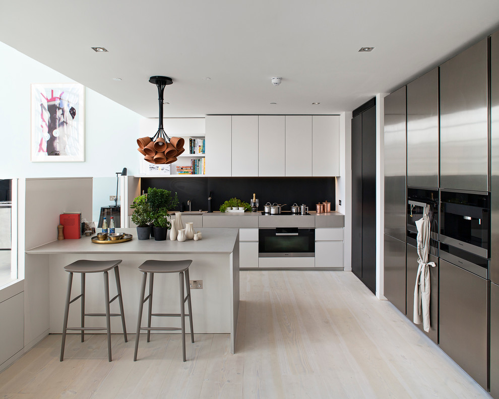 Große Skandinavische Küchenbar in L-Form mit flächenbündigen Schrankfronten, Küchenrückwand in Schwarz, Elektrogeräten mit Frontblende, hellem Holzboden und Kücheninsel in London