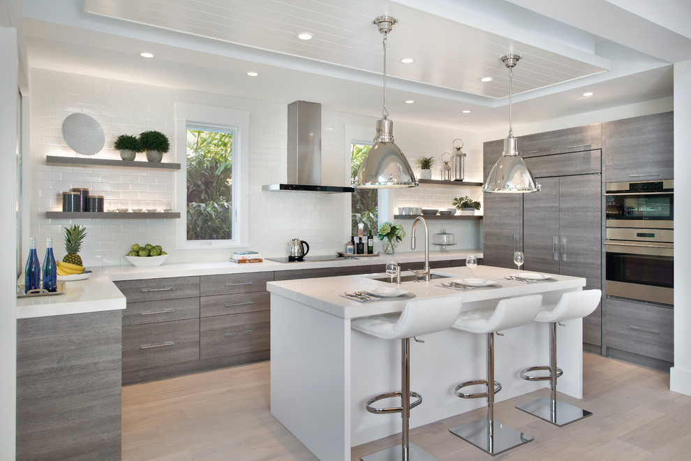 Contemporary l-shaped kitchen in Miami with a submerged sink, flat-panel cabinets, white splashback, ceramic splashback, integrated appliances, light hardwood flooring and an island.