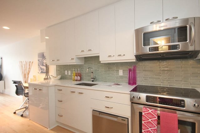 Modern inredning av ett litet kök, med en undermonterad diskho, släta luckor, vita skåp, grått stänkskydd, stänkskydd i glaskakel, rostfria vitvaror, ljust trägolv, bänkskiva i kvartsit och beiget golv