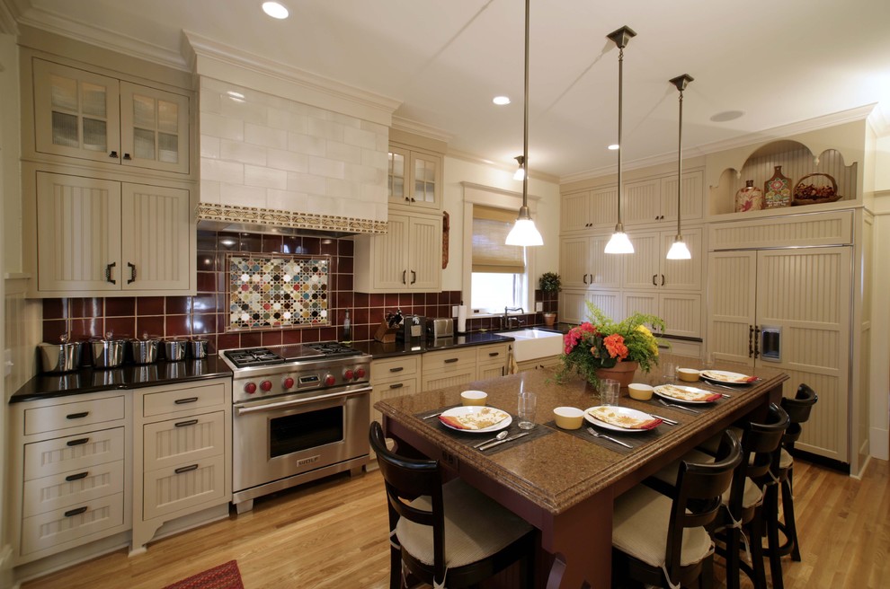 Klassisk inredning av ett kök, med integrerade vitvaror, en rustik diskho, luckor med infälld panel, beige skåp, rött stänkskydd och stänkskydd i keramik