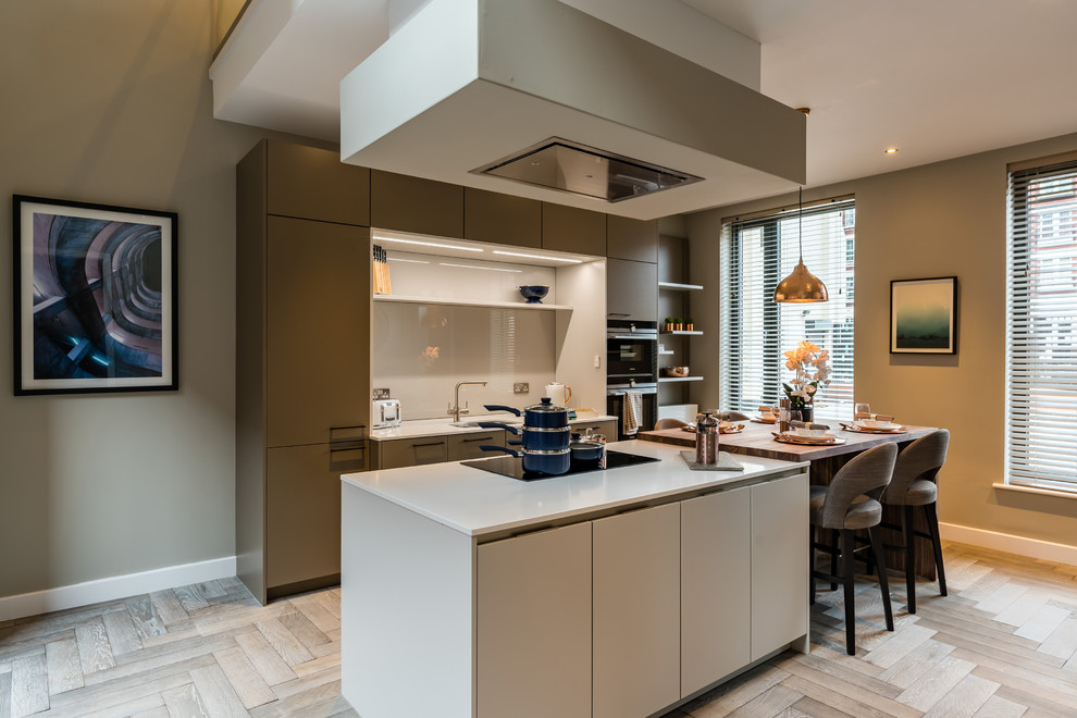 Aménagement d'une cuisine américaine parallèle moderne avec un placard à porte plane, des portes de placard grises, une crédence grise, un électroménager noir, parquet clair, îlot et un sol beige.