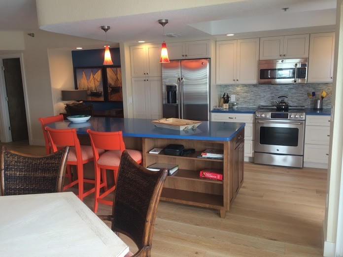 Bild på ett maritimt kök och matrum, med vita skåp, rostfria vitvaror, en köksö, flerfärgad stänkskydd och stänkskydd i glaskakel