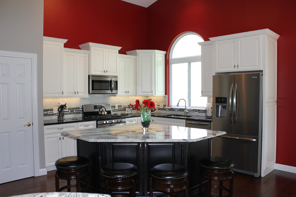 Mid-sized elegant l-shaped dark wood floor eat-in kitchen photo in St Louis with an undermount sink, raised-panel cabinets, white cabinets, quartz countertops, white backsplash, glass tile backsplash, stainless steel appliances and an island