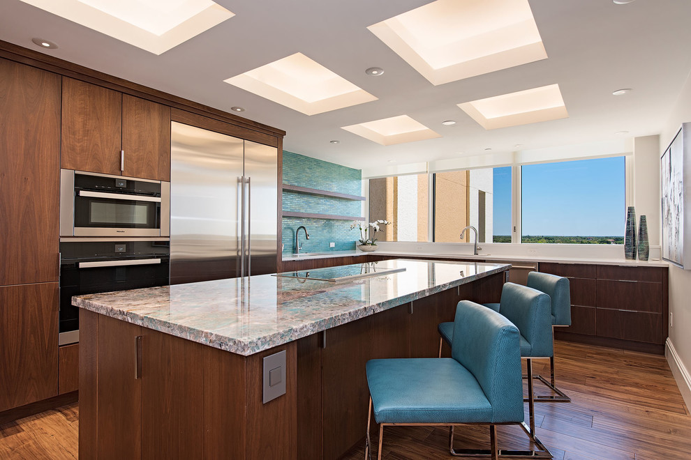 Moderne Küche in L-Form mit flächenbündigen Schrankfronten, dunklen Holzschränken, Küchenrückwand in Grün, Küchengeräten aus Edelstahl, braunem Holzboden, Kücheninsel und bunter Arbeitsplatte in Miami
