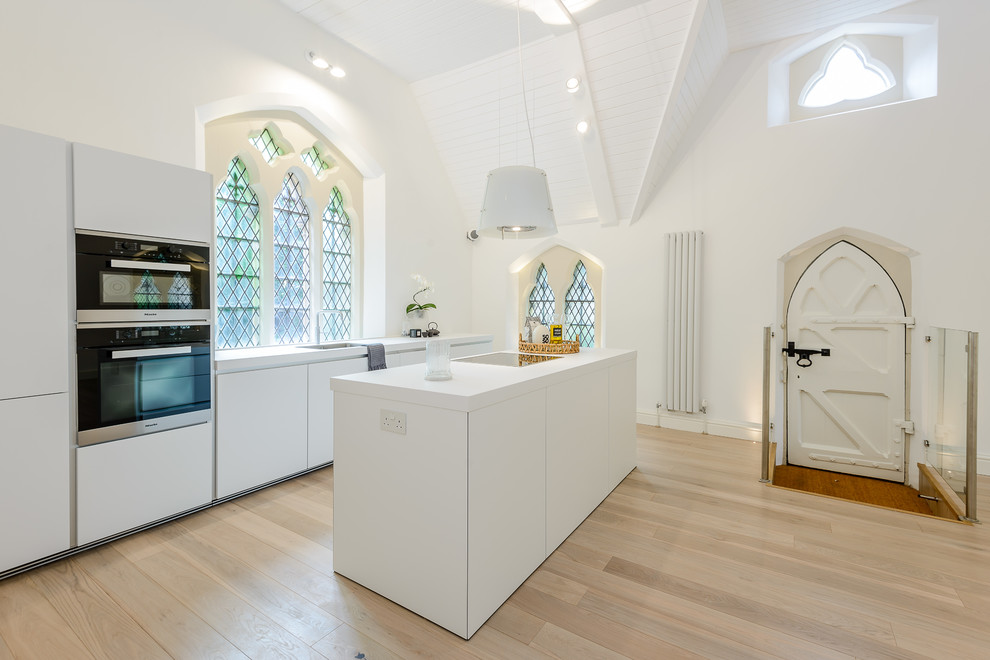 This is an example of a medium sized eclectic single-wall open plan kitchen in Hampshire with a submerged sink, flat-panel cabinets, white cabinets, an island, beige floors, white worktops and light hardwood flooring.