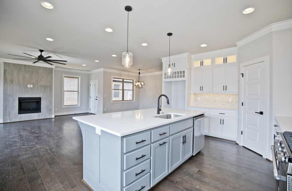 Modern inredning av ett mellanstort vit vitt kök, med en undermonterad diskho, luckor med infälld panel, vita skåp, bänkskiva i kvarts, vitt stänkskydd, stänkskydd i mosaik, rostfria vitvaror, mellanmörkt trägolv, en köksö och brunt golv