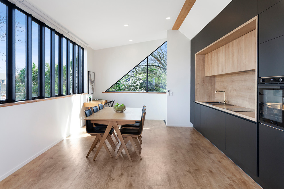 Design ideas for a contemporary single-wall kitchen/diner in Christchurch with a built-in sink, flat-panel cabinets, black cabinets, brown splashback, black appliances, brown floors and brown worktops.