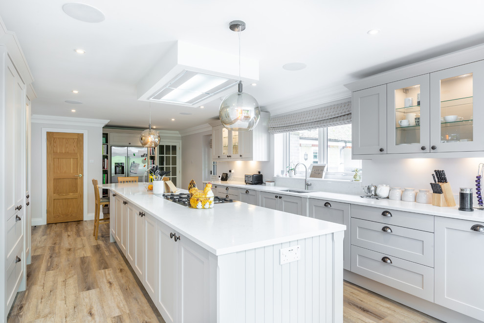 Inspiration for a large classic galley kitchen/diner in Sussex with shaker cabinets, grey cabinets, quartz worktops, an island, white worktops, a submerged sink, white splashback, integrated appliances, medium hardwood flooring and brown floors.