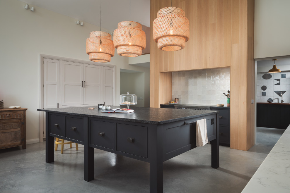 Photo of a rural open plan kitchen in Other with beaded cabinets, black cabinets, white splashback, stainless steel appliances, concrete flooring, an island, grey floors and black worktops.