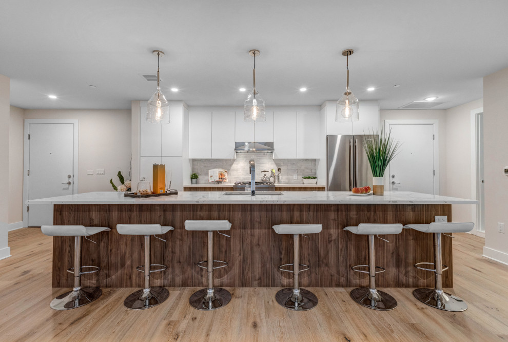 Inspiration for a large contemporary galley light wood floor and beige floor kitchen remodel in New York with an undermount sink, flat-panel cabinets, white cabinets, gray backsplash, stainless steel appliances, an island and white countertops