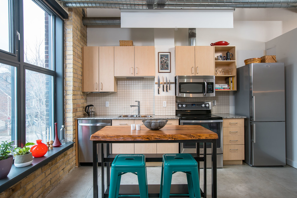 Immagine di una cucina industriale con lavello a doppia vasca, ante lisce, ante in legno chiaro, paraspruzzi bianco, elettrodomestici in acciaio inossidabile e pavimento in cemento