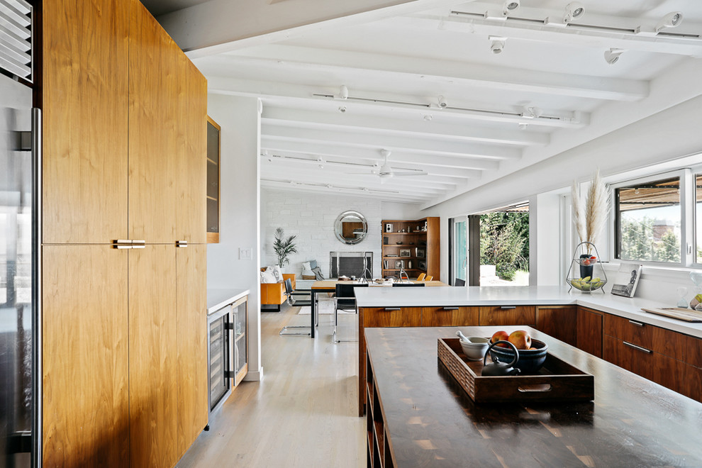 This is an example of a large retro u-shaped open plan kitchen in Los Angeles with a double-bowl sink, medium wood cabinets, wood worktops, white splashback, stainless steel appliances, light hardwood flooring, an island, beige floors and white worktops.