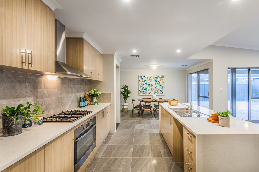 Immagine di un cucina con isola centrale minimal con ante lisce, ante in legno chiaro, paraspruzzi grigio, elettrodomestici in acciaio inossidabile e pavimento grigio