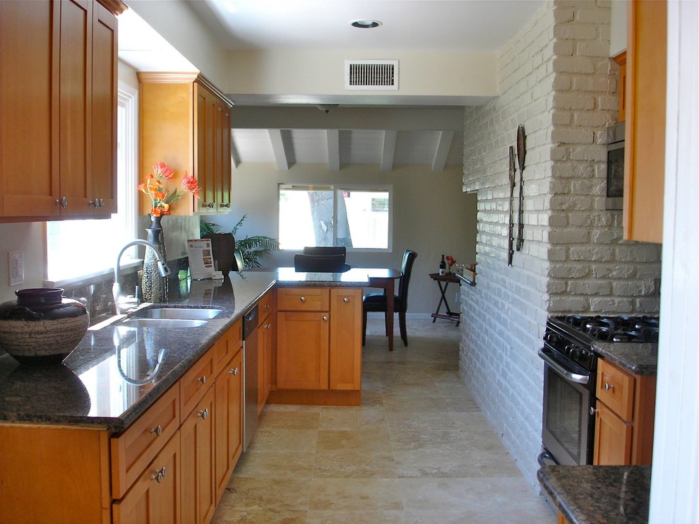 Medium sized traditional l-shaped kitchen/diner in Los Angeles with a double-bowl sink, shaker cabinets, medium wood cabinets, granite worktops, stainless steel appliances, porcelain flooring, a breakfast bar, brown floors and black worktops.