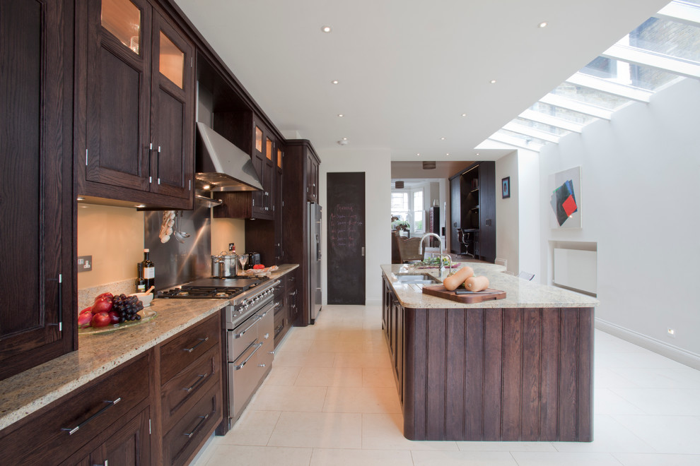 Klassisk inredning av ett stort kök, med luckor med infälld panel, granitbänkskiva, rostfria vitvaror, en köksö, en dubbel diskho, skåp i mörkt trä, stänkskydd med metallisk yta och stänkskydd i metallkakel