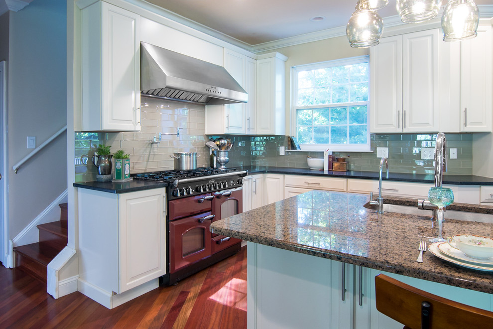 Example of a huge classic l-shaped medium tone wood floor open concept kitchen design in Philadelphia with an undermount sink, raised-panel cabinets, white cabinets, granite countertops, green backsplash, glass tile backsplash, stainless steel appliances, an island and multicolored countertops
