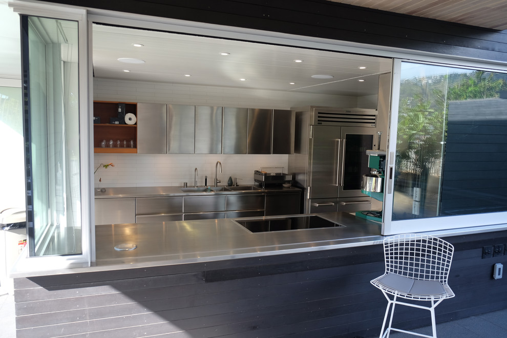 Bild på ett mellanstort funkis kök, med en integrerad diskho, släta luckor, skåp i rostfritt stål, bänkskiva i rostfritt stål, vitt stänkskydd, stänkskydd i glaskakel, rostfria vitvaror och klinkergolv i porslin