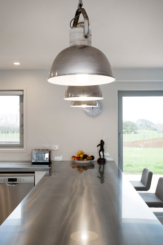 Example of a large minimalist u-shaped porcelain tile open concept kitchen design in Auckland with a double-bowl sink, flat-panel cabinets, white cabinets, stainless steel countertops, white backsplash, glass sheet backsplash, stainless steel appliances and a peninsula