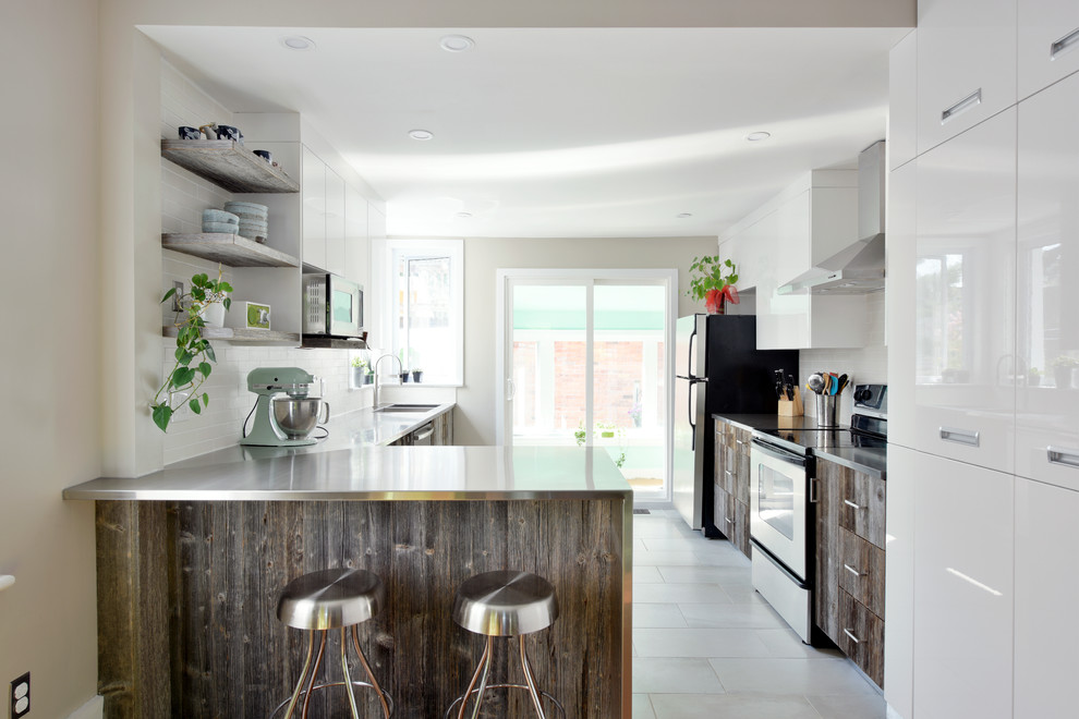 Medium sized contemporary l-shaped kitchen in Ottawa with stainless steel worktops, an integrated sink, flat-panel cabinets, distressed cabinets, white splashback, metro tiled splashback, stainless steel appliances, porcelain flooring and a breakfast bar.