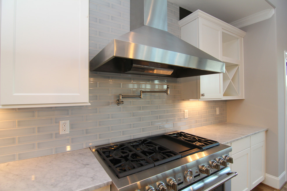 Inredning av ett modernt stort kök, med en enkel diskho, luckor med infälld panel, vita skåp, granitbänkskiva, blått stänkskydd, stänkskydd i keramik, rostfria vitvaror, ljust trägolv och en köksö