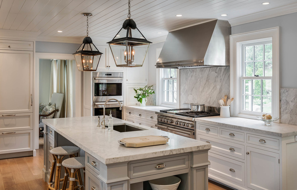 Example of a transitional l-shaped light wood floor kitchen design in New York with an undermount sink, recessed-panel cabinets, white cabinets, gray backsplash, stone slab backsplash, stainless steel appliances and an island