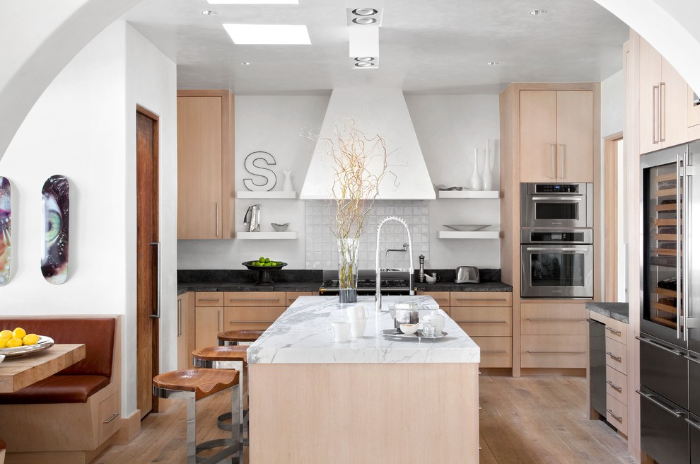 Mediterranean kitchen in Austin with flat-panel cabinets, light wood cabinets, white splashback, stainless steel appliances, medium hardwood flooring and an island.