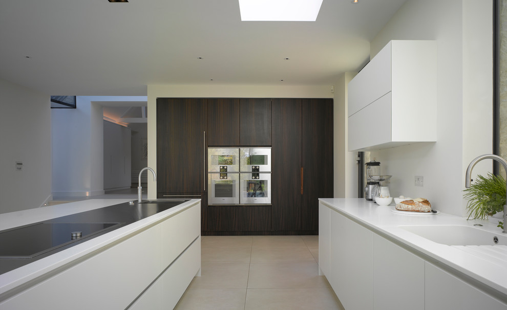 Design ideas for an expansive contemporary single-wall open plan kitchen in London with flat-panel cabinets, white cabinets, composite countertops, metallic splashback, mirror splashback, ceramic flooring, an island, white floors and white worktops.