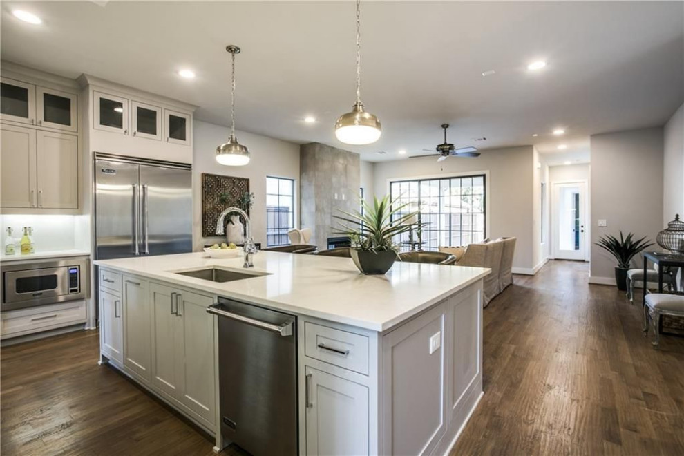 Mid-sized transitional medium tone wood floor and brown floor open concept kitchen photo in Dallas with a single-bowl sink, recessed-panel cabinets, gray cabinets, quartzite countertops, white backsplash, porcelain backsplash, stainless steel appliances, an island and white countertops