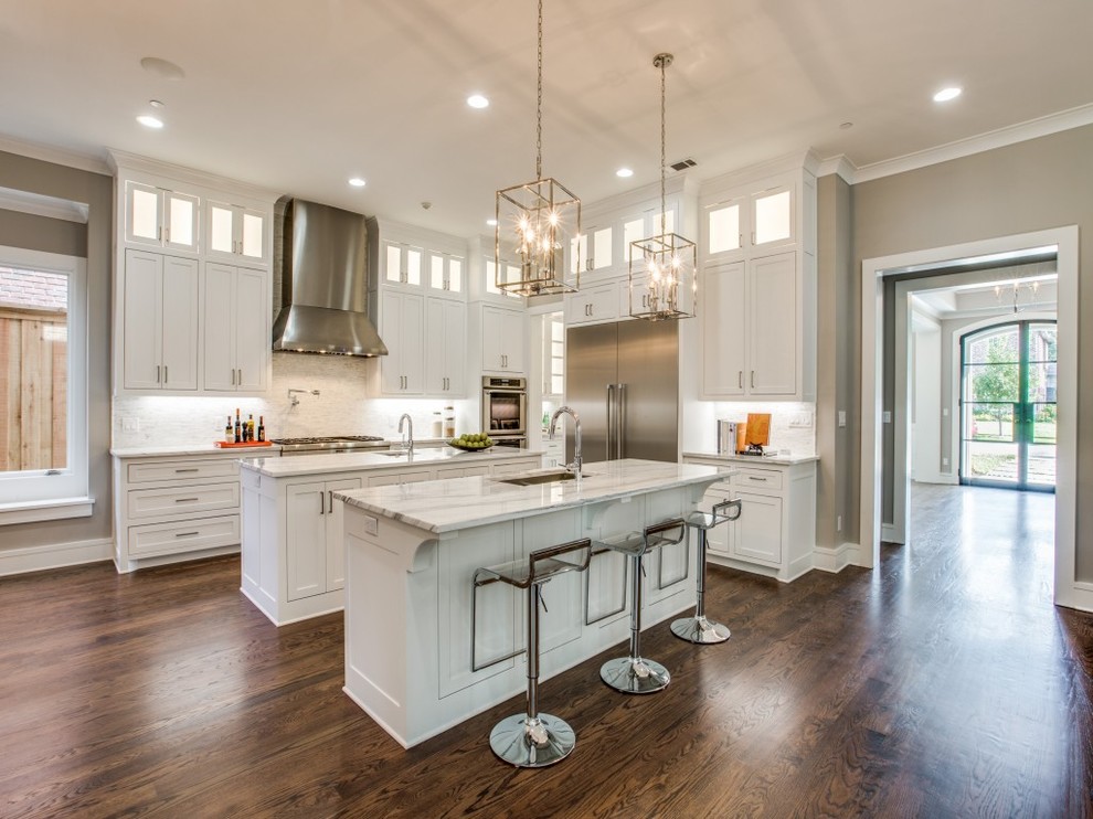 Photo of a large traditional l-shaped enclosed kitchen in Dallas with a submerged sink, recessed-panel cabinets, white cabinets, marble worktops, white splashback, marble splashback, stainless steel appliances, dark hardwood flooring, multiple islands, brown floors and white worktops.