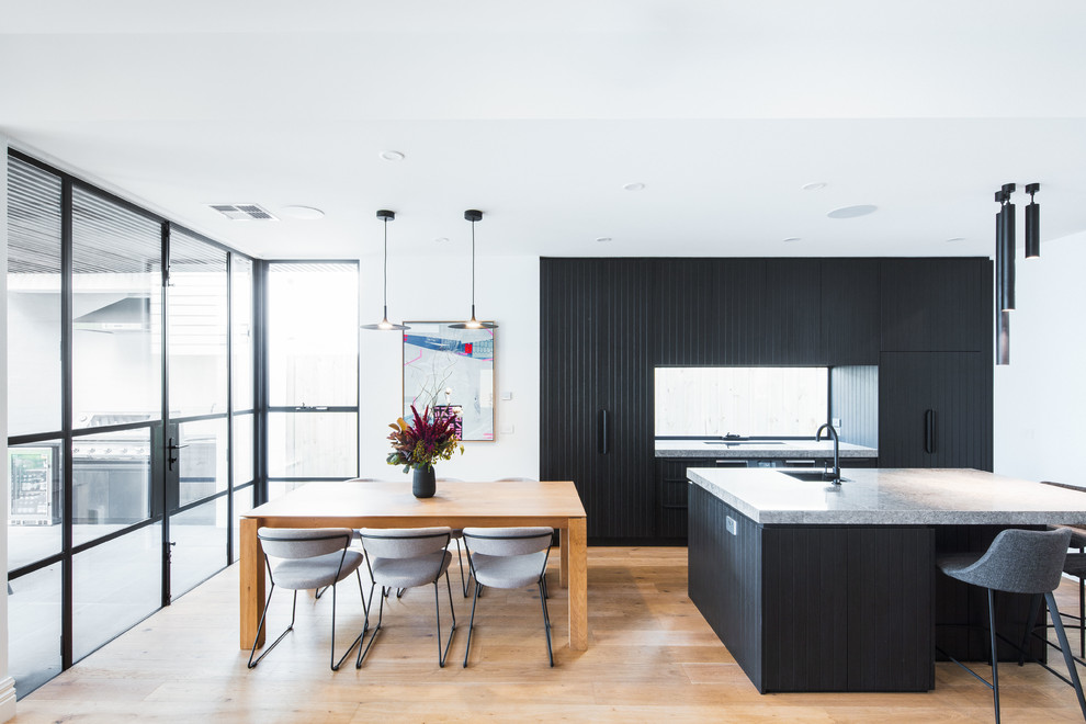 Example of a mid-sized trendy galley medium tone wood floor and brown floor open concept kitchen design in Melbourne with black cabinets, quartz countertops, window backsplash, black appliances, an island, gray countertops, an undermount sink and flat-panel cabinets