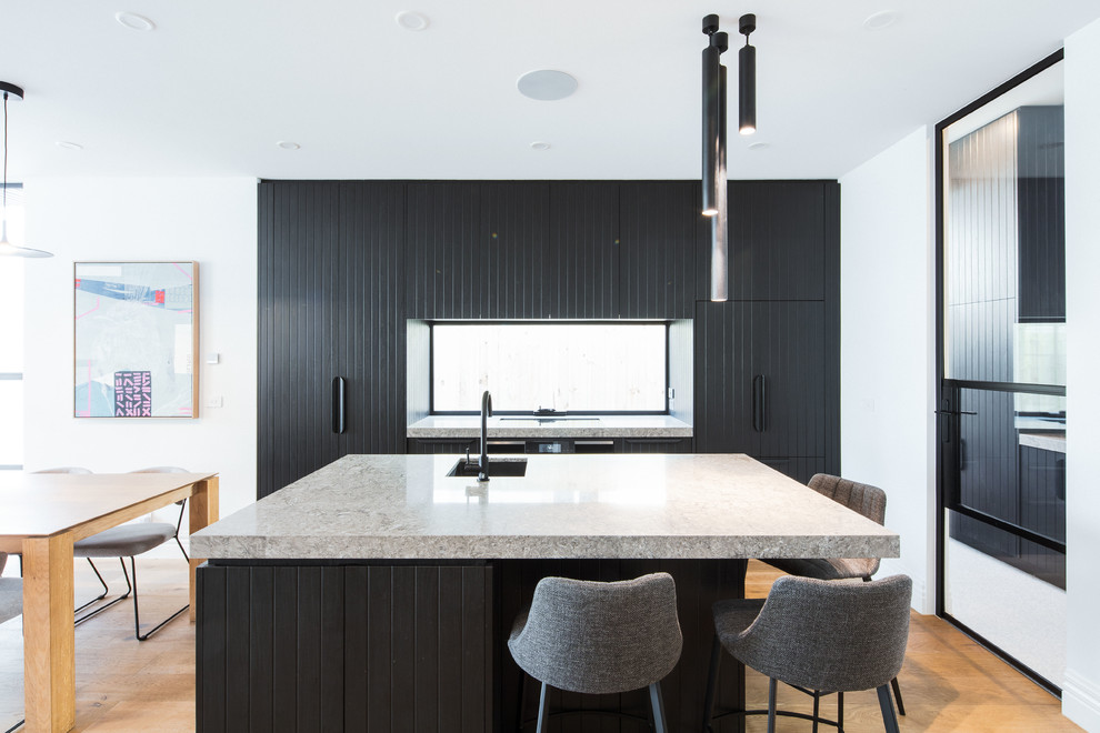 Photo of a medium sized contemporary kitchen/diner in Melbourne with a submerged sink, black cabinets, engineered stone countertops, window splashback, black appliances, light hardwood flooring, an island and grey worktops.