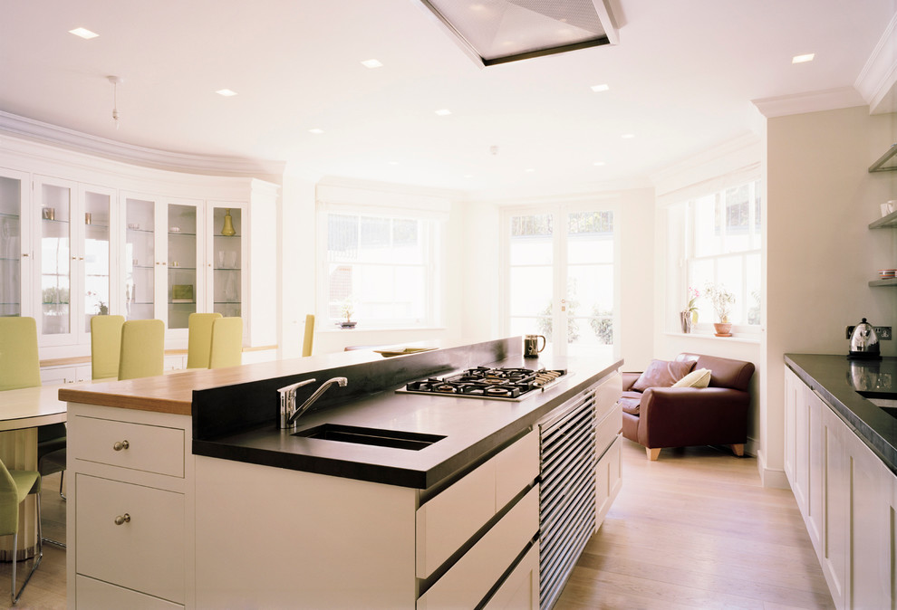 This is an example of a bohemian kitchen in London with a submerged sink, shaker cabinets, white cabinets, granite worktops, stainless steel appliances, medium hardwood flooring and an island.