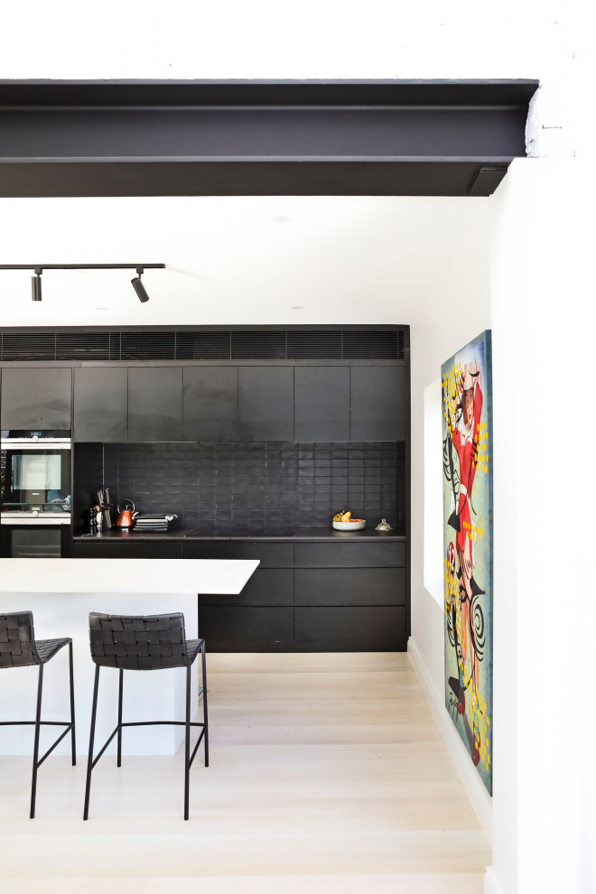 Photo of a contemporary galley kitchen in Sydney with flat-panel cabinets, black splashback, stainless steel appliances, light hardwood flooring, an island, beige floors and black worktops.