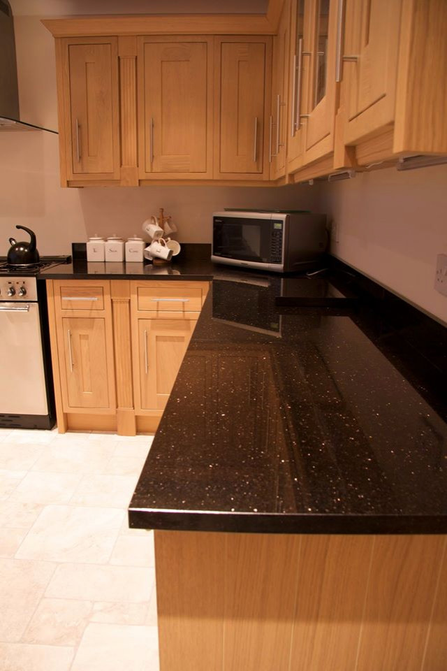 This is an example of a modern l-shaped kitchen in West Midlands with light wood cabinets, black worktops and granite worktops.