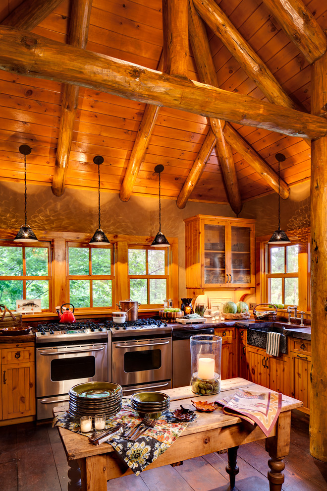 Foto på ett rustikt kök, med en rustik diskho, skåp i mellenmörkt trä, fönster som stänkskydd, rostfria vitvaror, en köksö, mörkt trägolv och brunt golv