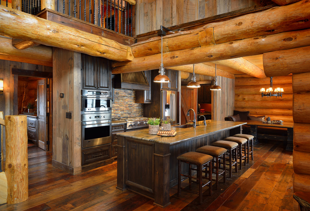 This is an example of a rustic galley open plan kitchen in Minneapolis with dark wood cabinets, multi-coloured splashback, stainless steel appliances and brown floors.